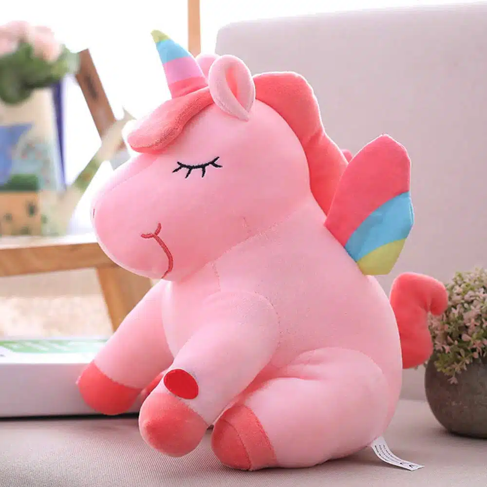 PELUCHE LICORNE LUMINEUSE ROSE AILÉE 4 UNE PELUCHE LICORNE LUMINEUSE ROSEE AILÉE SUR UN CANAPÉ