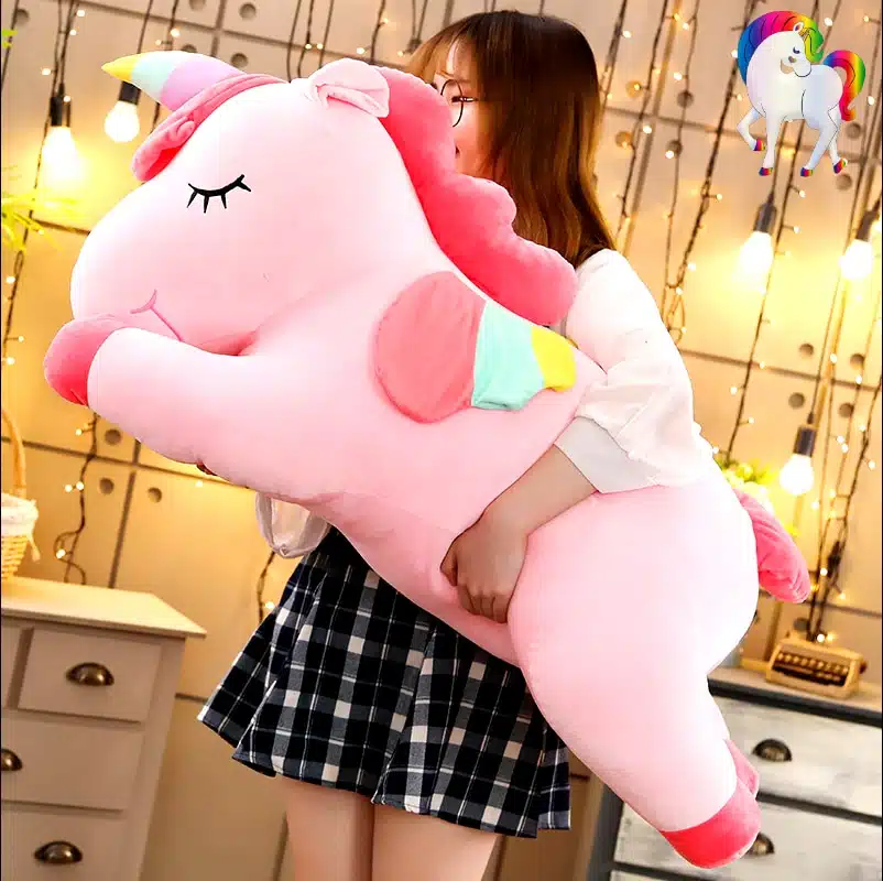 PELUCHE LICORNE GÉANTE ROSE AILÉE 8 JEUNE FILLE QUI TIENT UNE PELUCHE LICORNE GÉANTE ROSE AILÉE